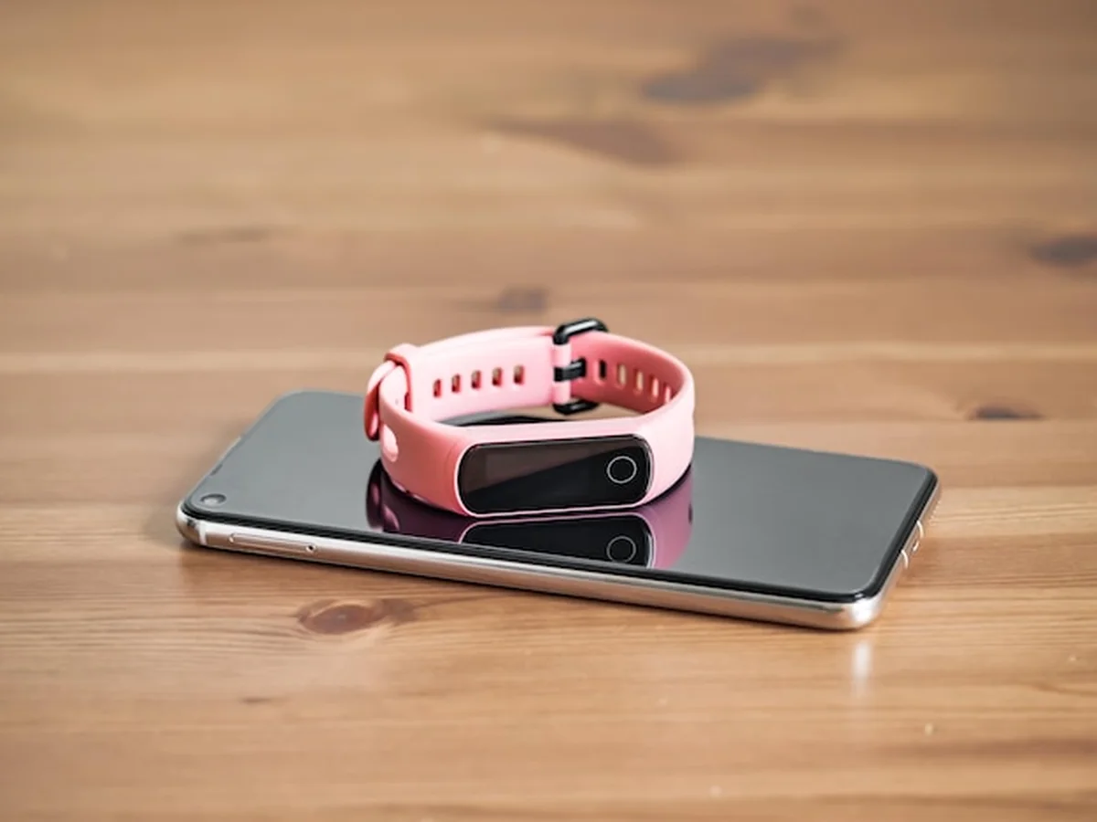 Fitness tracker różowy na drewnianym stole obok smartfona